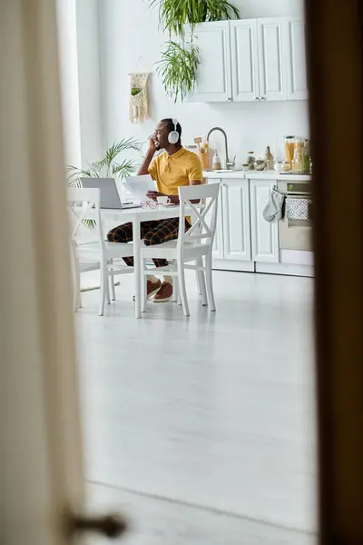 Um jovem afro-americano se concentra em seu trabalho remoto em uma cozinha elegante cheia de vegetação. — Fotografia de Stock
