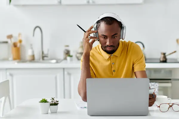 A focused young man in a yellow shirt engages with his laptop while working in a chic kitchen. — Stock Photo