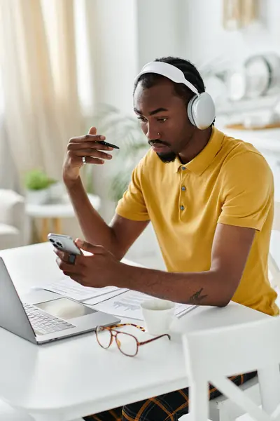 Focused young man collaborates remotely, using his phone and laptop in a bright, inviting workspace. — Stock Photo