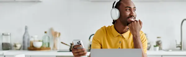 Confident young man uses laptop and phone while enjoying remote work in a modern kitchen. — Stock Photo