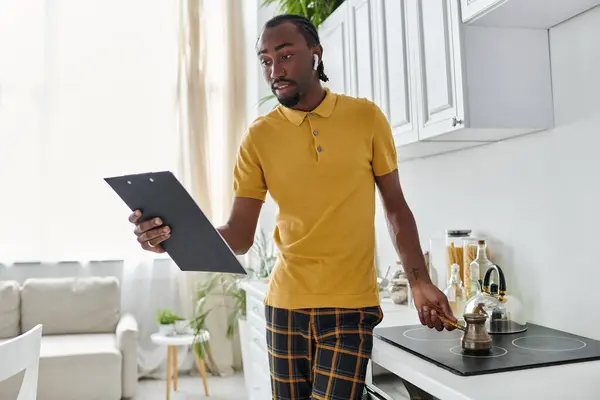 A young man reviews his tasks on a clipboard while brewing coffee in a stylish kitchen. — Stock Photo