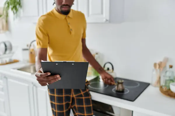 Ein junger Mann in einer stilvollen Küche überprüft ein Rezept bei der Zubereitung einer Mahlzeit und vereint Arbeit und Leben. — Stockfoto