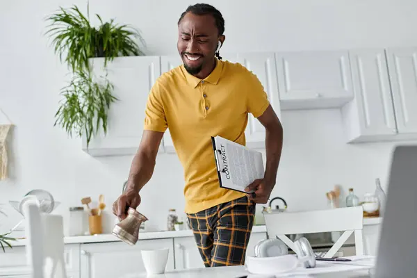 Un joven afroamericano prepara café mientras revisa sus notas de trabajo en una cocina luminosa. - foto de stock