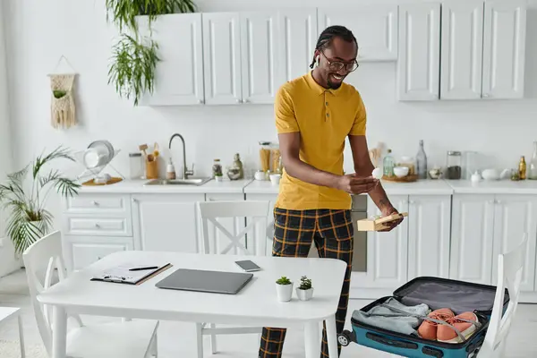 A young african american man eagerly packs his suitcase in a chic kitchen for remote work. — Stock Photo