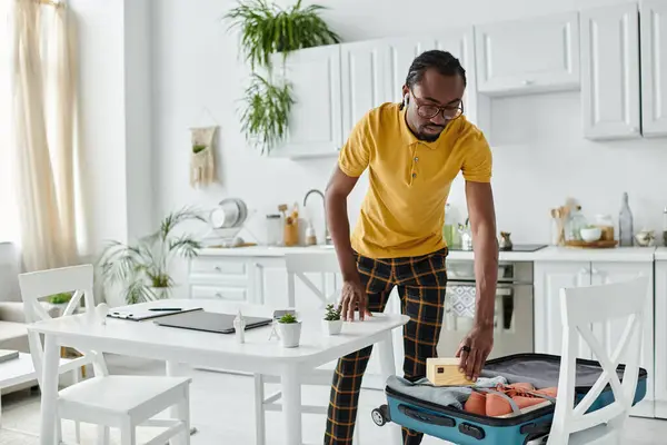 A stylish young man packs his suitcase, preparing for a new adventure while surrounded by plants. — Stock Photo