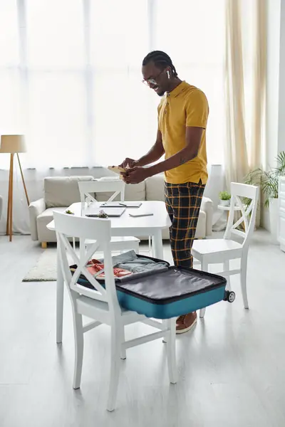 A young man packs his suitcase, balancing work and travel in a bright, modern space. — Stock Photo