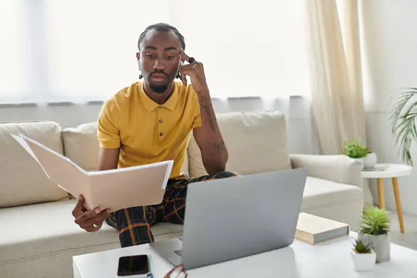 A young African American man reviews important documents while working remotely on his laptop. — Stock Photo