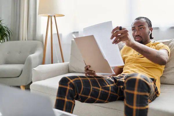 A young african american man engaged in remote work, examining important documents in comfort. — Stock Photo