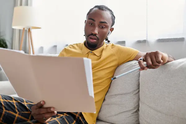 Young african american man sits comfortably on a couch, reviewing notes intently with a pen in hand. — Stock Photo