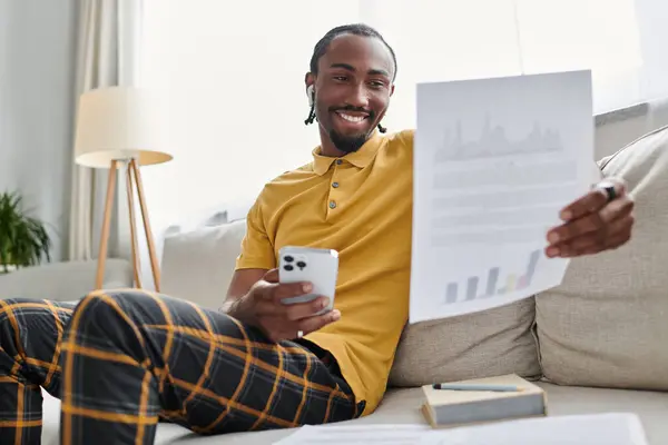 A smiling young african american man reviews documents on his couch, balancing work and comfort. — Stock Photo