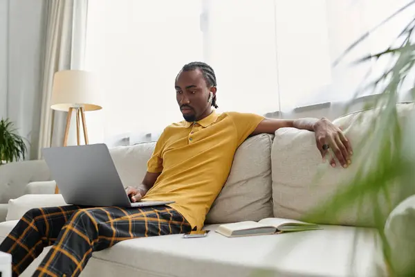 A digital nomad works on his laptop, lounging on a sofa amidst greenery. — Stock Photo