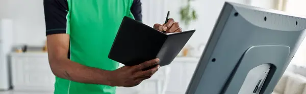 This young african american man engages in remote work, jotting down ideas in a notebook. — Stock Photo