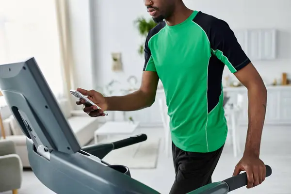 A young man works out on a treadmill in a bright, modern room, using his phone. — Stock Photo