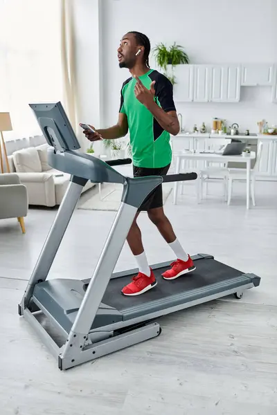 A motivated young man jogs on a treadmill at home during his work session. — Stock Photo