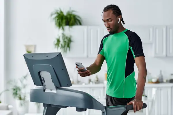 Young african american man exercises on a treadmill while checking messages on his smartphone. — Stock Photo