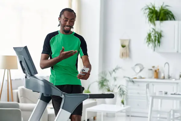 Engaged in fitness, a young man runs on a treadmill while using his phone in a stylish living space. — Stock Photo