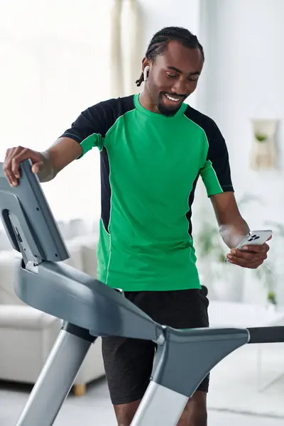 A young african american man exercises on a treadmill, engaging with his phone in a stylish setting. — Stock Photo