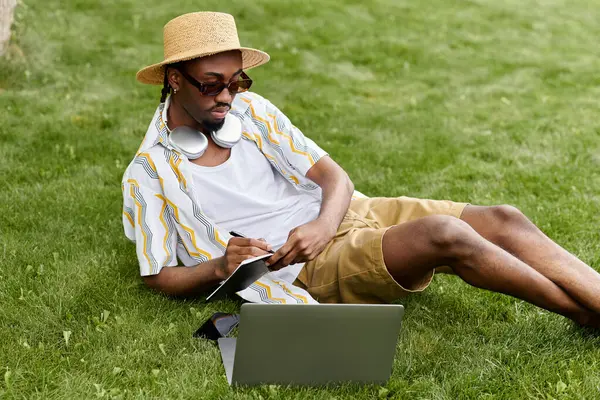 Man enjoys remote work on a laptop while relaxing on grass, balancing comfort and productivity. — Stock Photo