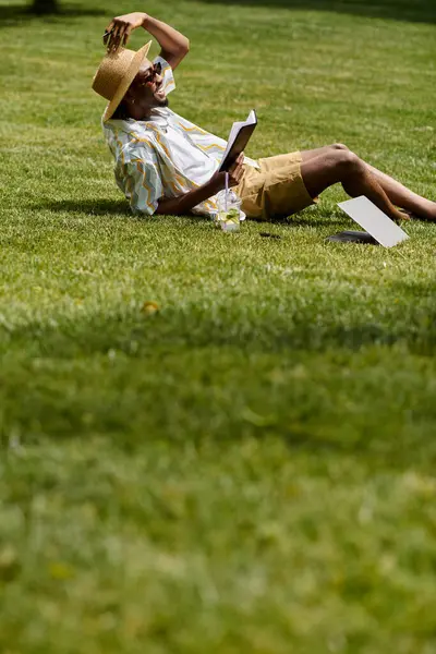 Relaxed digital nomad reads and works under the sun, surrounded by lush green grass and nature. — Stock Photo