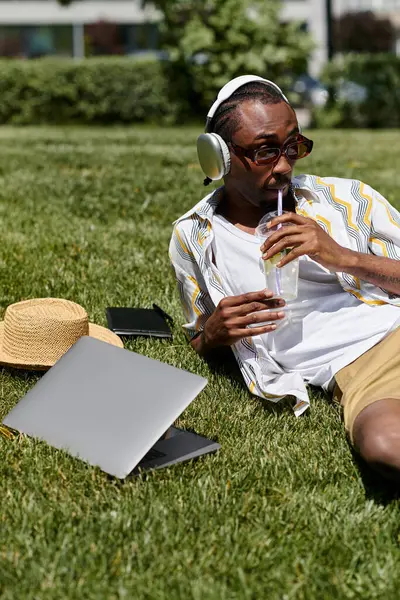 Casual workday in the park for a young man, relishing a drink and music in natures tranquility. — Stock Photo