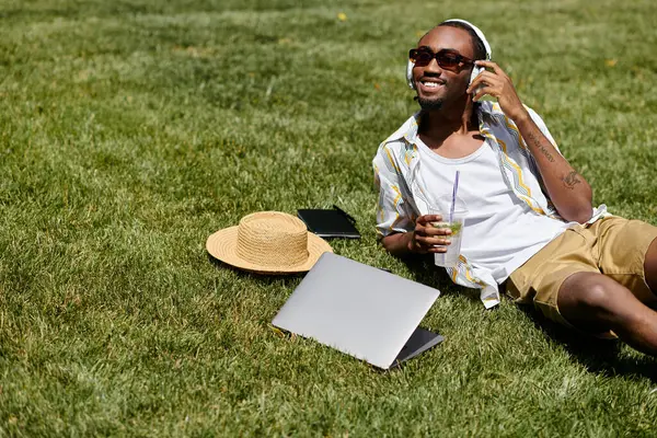 A young African American man relaxes in a grassy park, enjoying his remote work routine. — Stock Photo