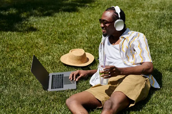 A young african american man relaxes on the grass, working with joy in a peaceful park setting. — Stock Photo