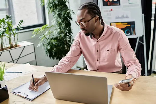 A young man diligently writes in his notebook while working remotely in a bright workspace. — Stock Photo