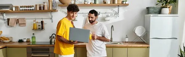 Two men enjoy each others company in their stylish kitchen while looking at a laptop, banner — Stock Photo
