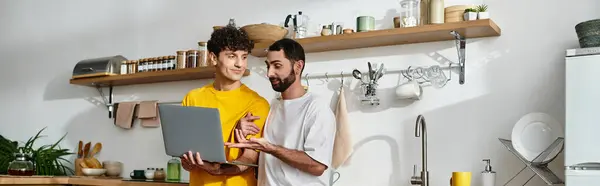 Deux hommes passent du bon temps ensemble à la maison, partageant sourires et rires tout en utilisant un ordinateur portable, bannière — Photo de stock