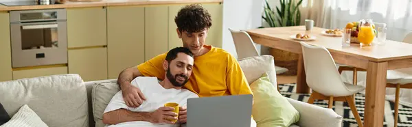 Two men relax on the couch, sharing affection while working on a laptop at home, banner — Stock Photo