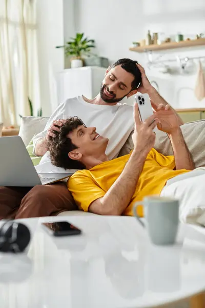 Dos hombres se relajan juntos en un sofá acogedor, acariciando su conexión en un ambiente de casa con estilo. - foto de stock