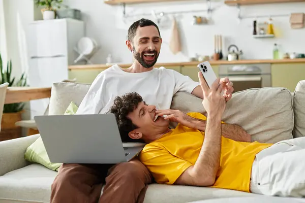 Two men relax on a couch, laughing together while enjoying tech in their stylish home. — Stock Photo