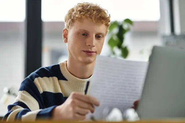 Focused young man in a striped sweater reviews important documents at work. — Stock Photo