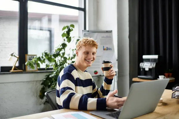 Un jeune rouquin en pull rayé sourit en travaillant sur son ordinateur portable dans un bureau contemporain. — Photo de stock