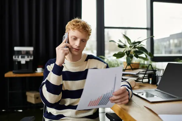 A young redhead man works on a report and speaks on the phone in a corporate office environment. — Stock Photo