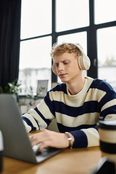 Young redhead man engages deeply with his laptop in a bright office environment. — Stock Photo