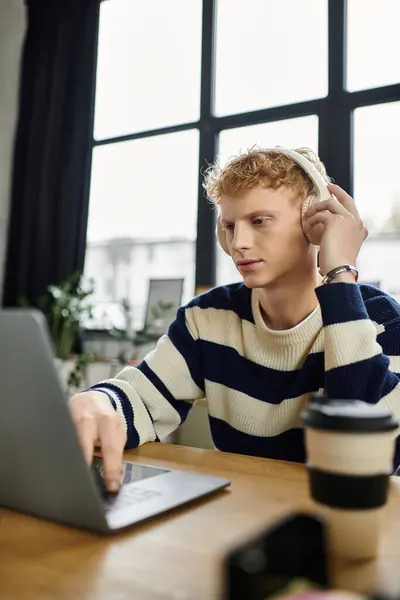 A focused young man in a striped sweater engages with his laptop while listening to music. — Stock Photo