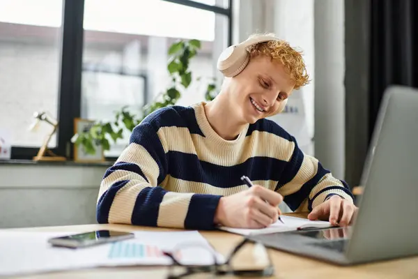 A young man in a striped sweater smiles as he works in a modern office. — Stock Photo