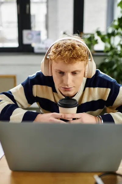 Focalisé jeune homme travaille intensément sur son ordinateur portable tout en sirotant du café dans un espace de travail élégant. — Photo de stock