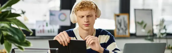 A young redhead in a striped sweater focuses on his tasks in an office, banner — Stock Photo
