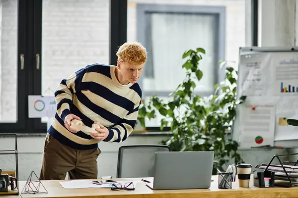 A young man in a striped sweater focuses on his work in an office filled with greenery. — Stock Photo