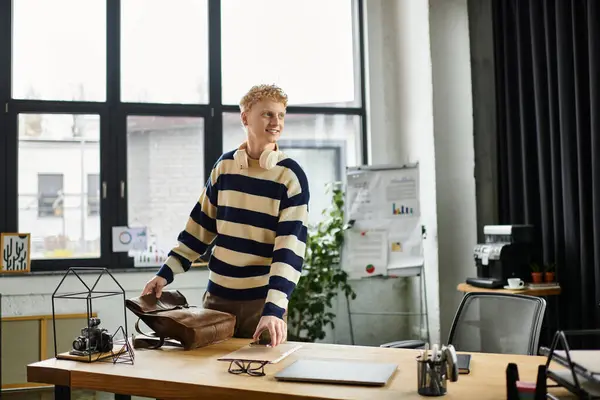 Young man in a striped sweater smiles while organizing his workspace in a modern office. — Stock Photo