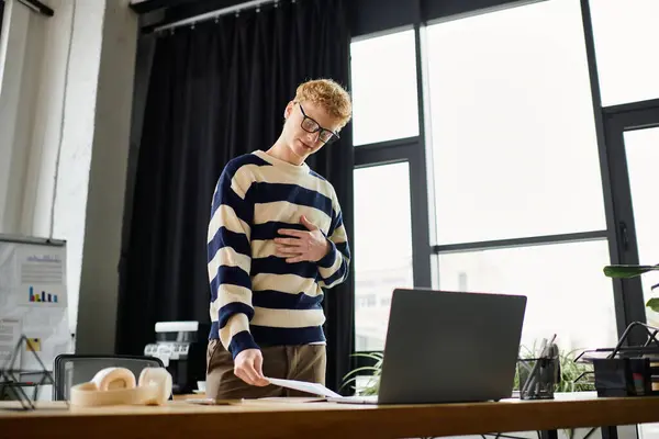 A young man with red hair in a striped sweater reviews papers in a stylish office setting. — Stock Photo