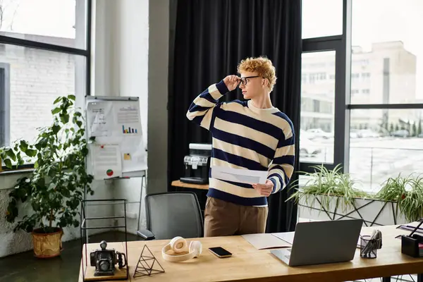 A young professional in a striped sweater thoughtfully reviews documents in a modern office. — Stock Photo