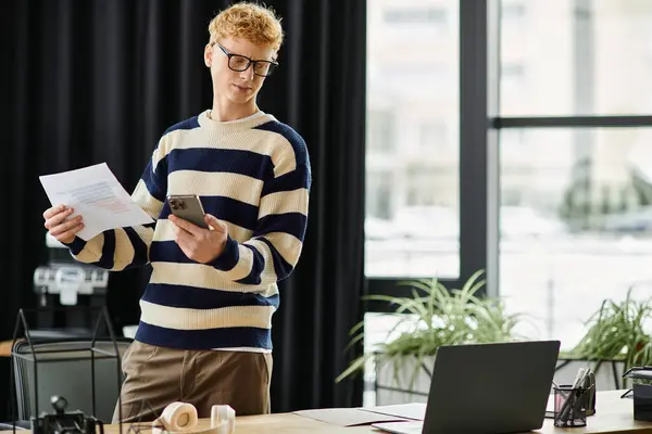 Engaged young man assesses documents while using his smartphone in a sleek office setting. — Stock Photo