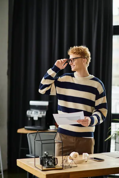 A young professional with red hair reviews documents while standing in a modern office setting. — Stock Photo
