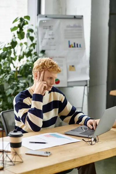 Young man in a striped sweater engages thoughtfully with his laptop in a bright office. — Stock Photo