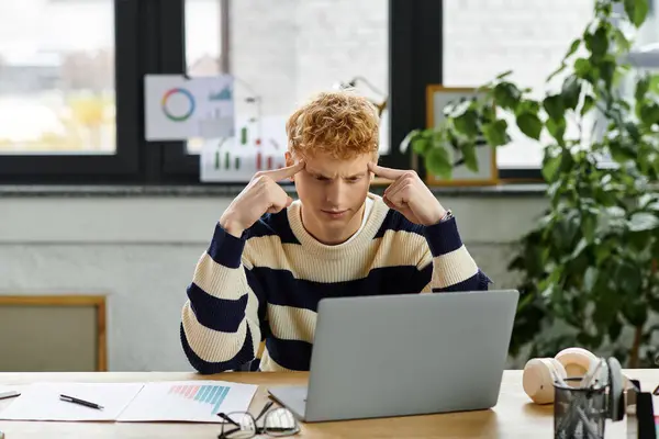 Jovem ruiva homem em uma camisola listrada se concentra em seu laptop em um ambiente corporativo. — Fotografia de Stock