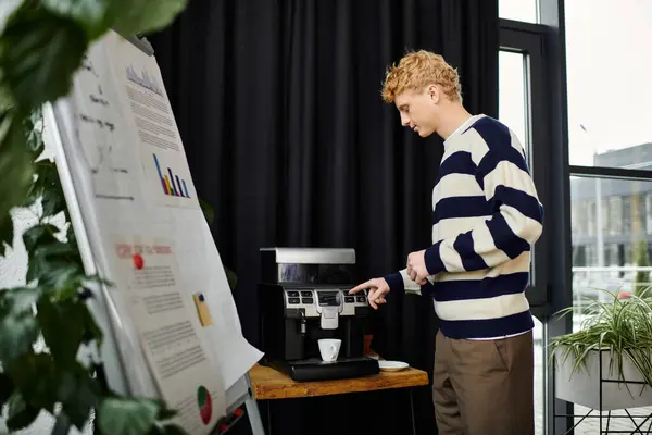 A young redhead man in a striped sweater prepares coffee in a sleek office space. — Stock Photo