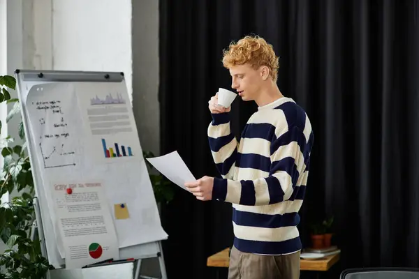 Redhead man in a striped sweater reviews documents while enjoying coffee at his corporate workspace. — Stock Photo